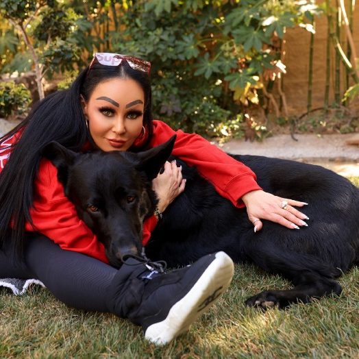 Lady sitting with her black German Shepherd on the ground hugging him
