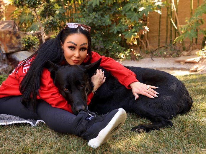 Lady sitting with her black German Shepherd on the ground hugging him