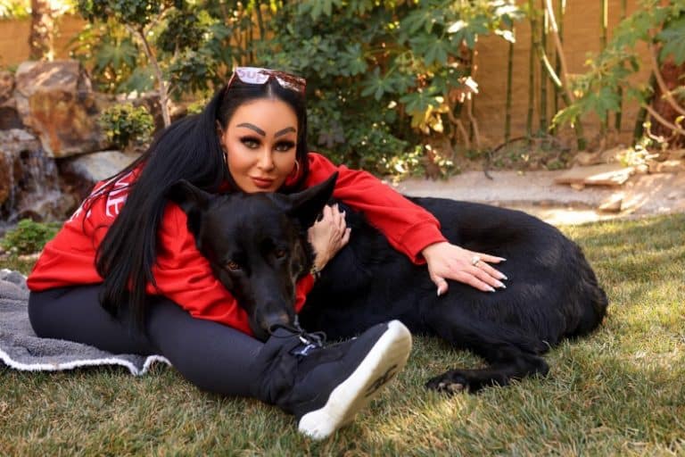 Lady sitting with her black German Shepherd on the ground hugging him